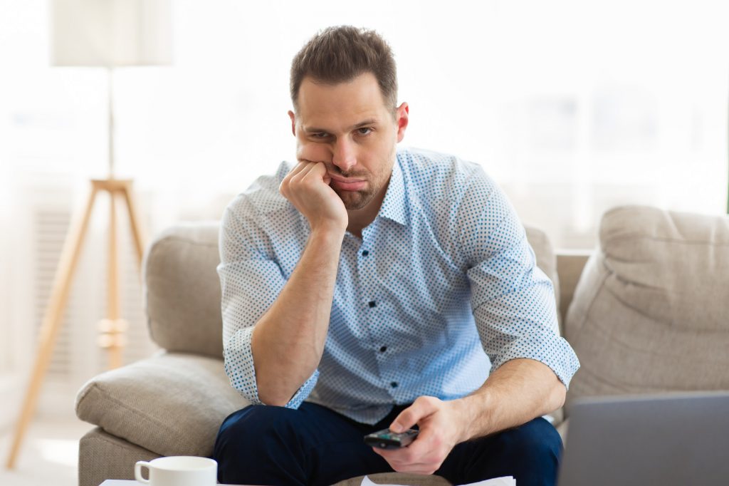 Tired man watching TV at home, holding remote control